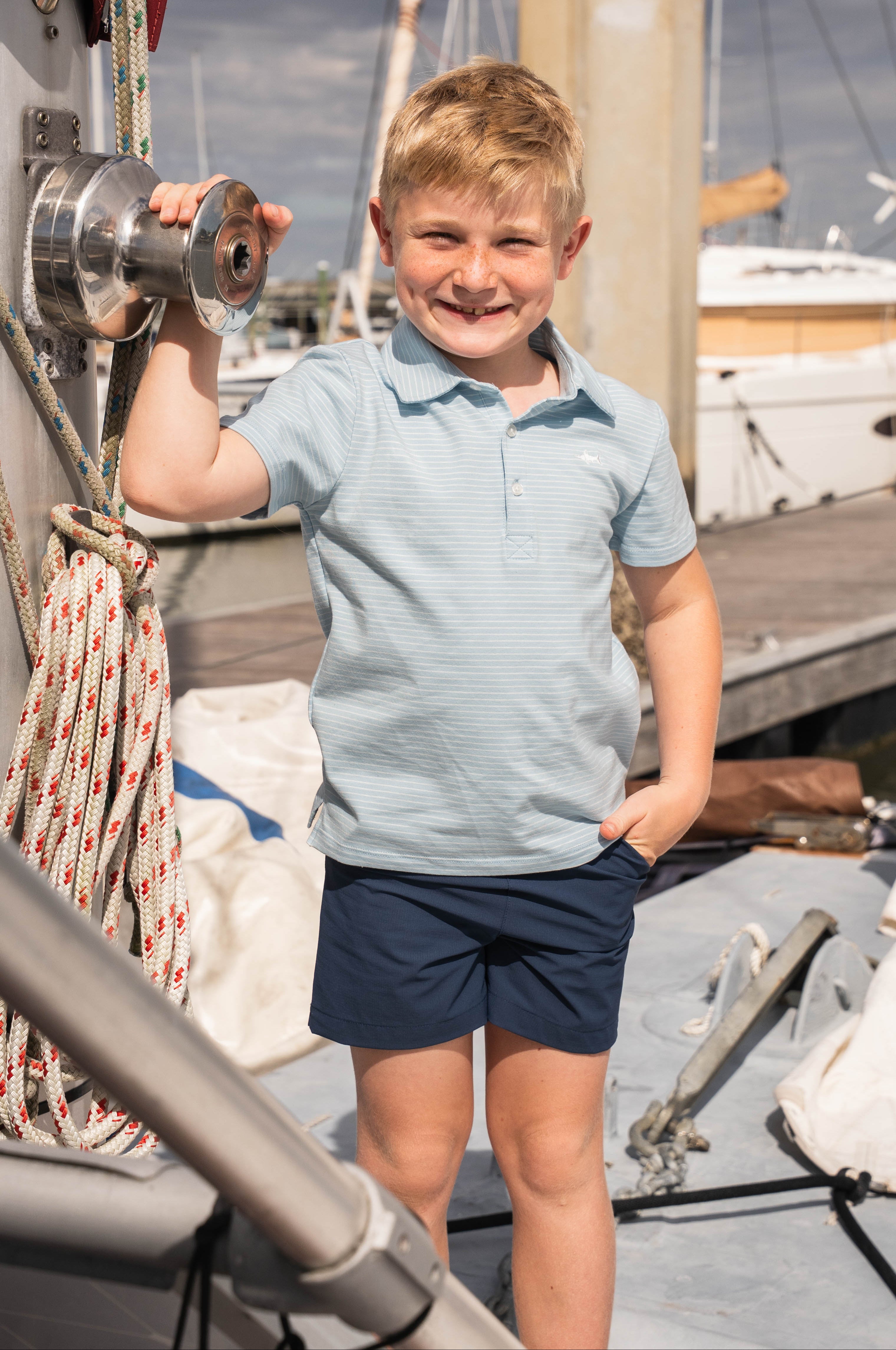 Young boy on a boat holding onto a metal railing with another boat in the background.