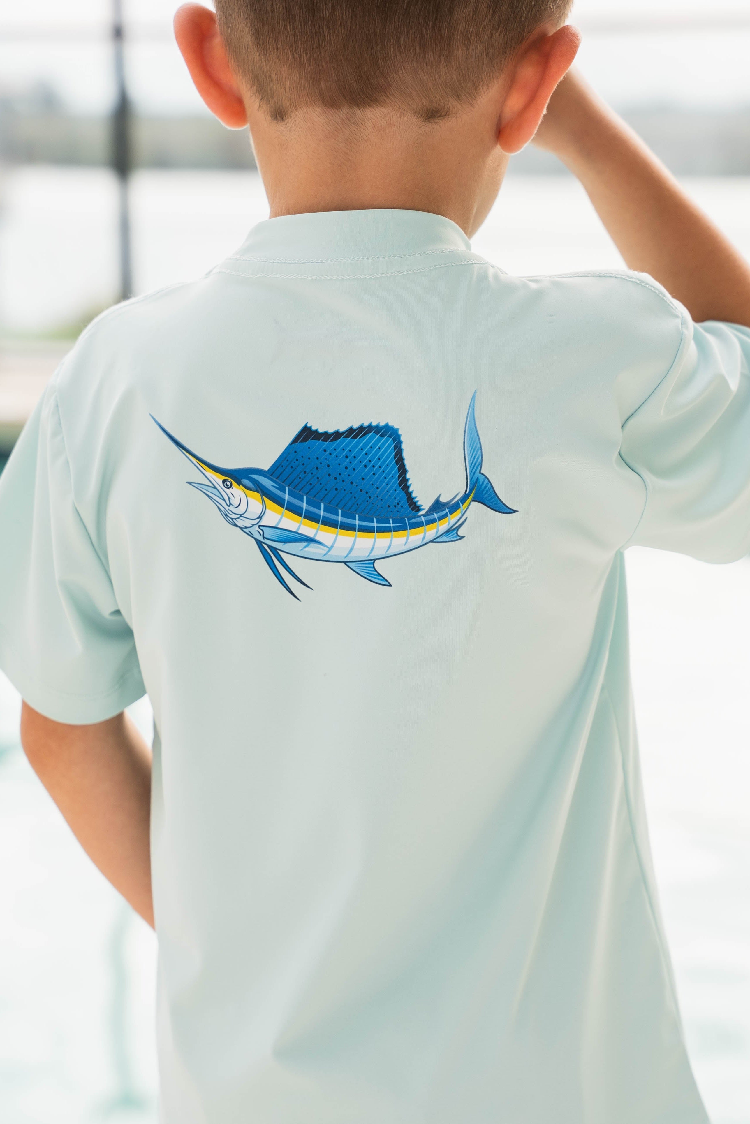 Child wearing a light blue t-shirt with a fish design by a pool