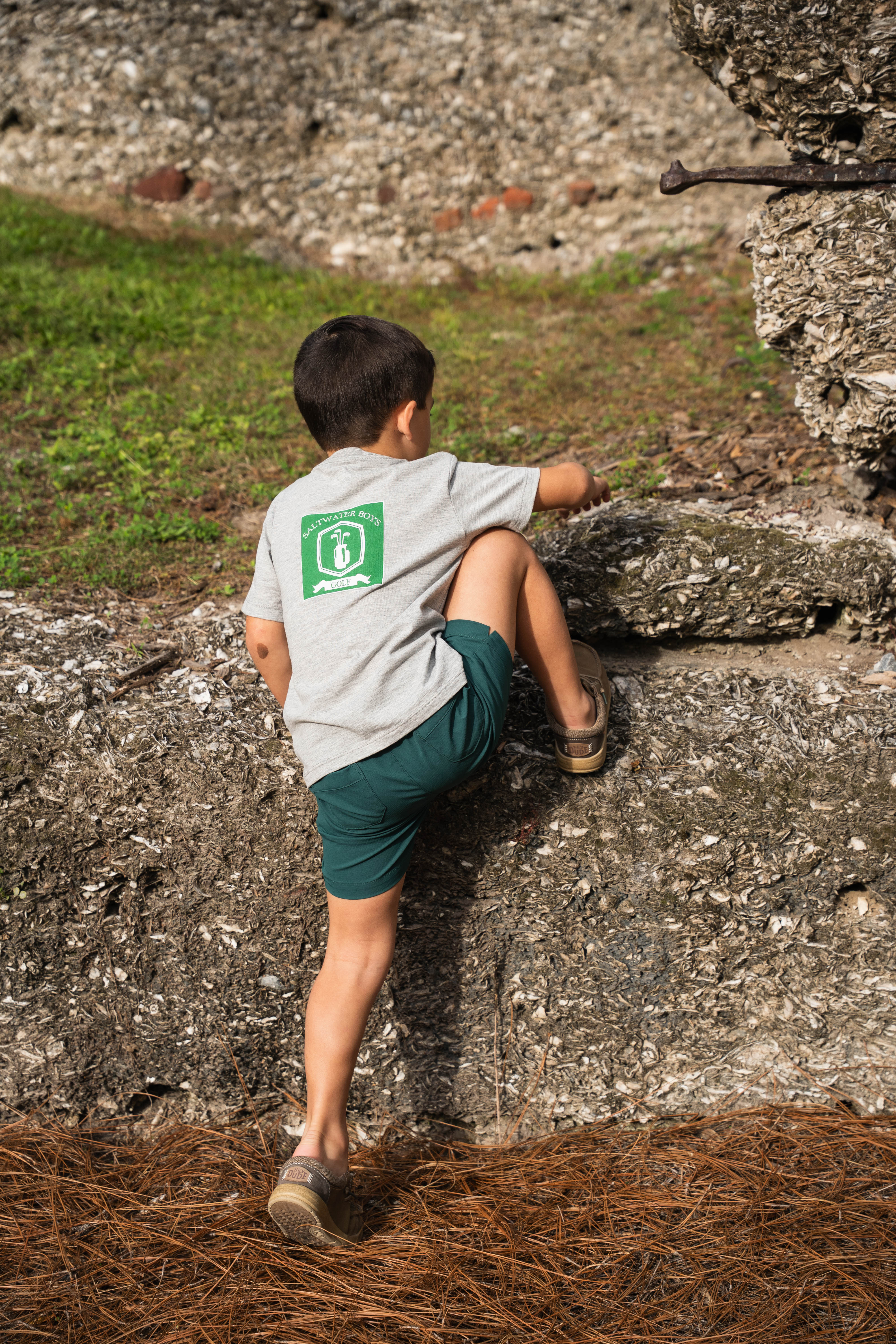 Child sitting on a stone wall with green grass and stone wall in the background